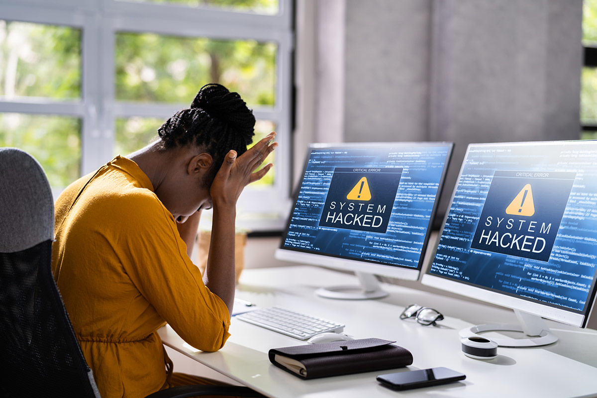 a woman sitting in front of computer monitors that say "system hacked"